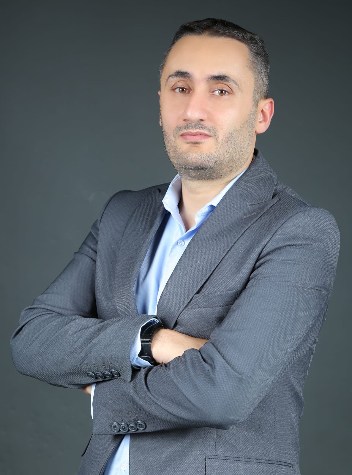 Alaa Husni Zeidan, MCIArb, arms crossed, in a grey suit